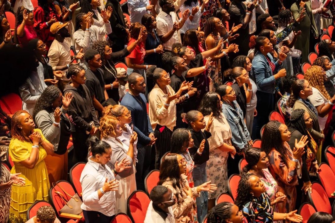 A Dominion City congregation standing in worship with hands raised